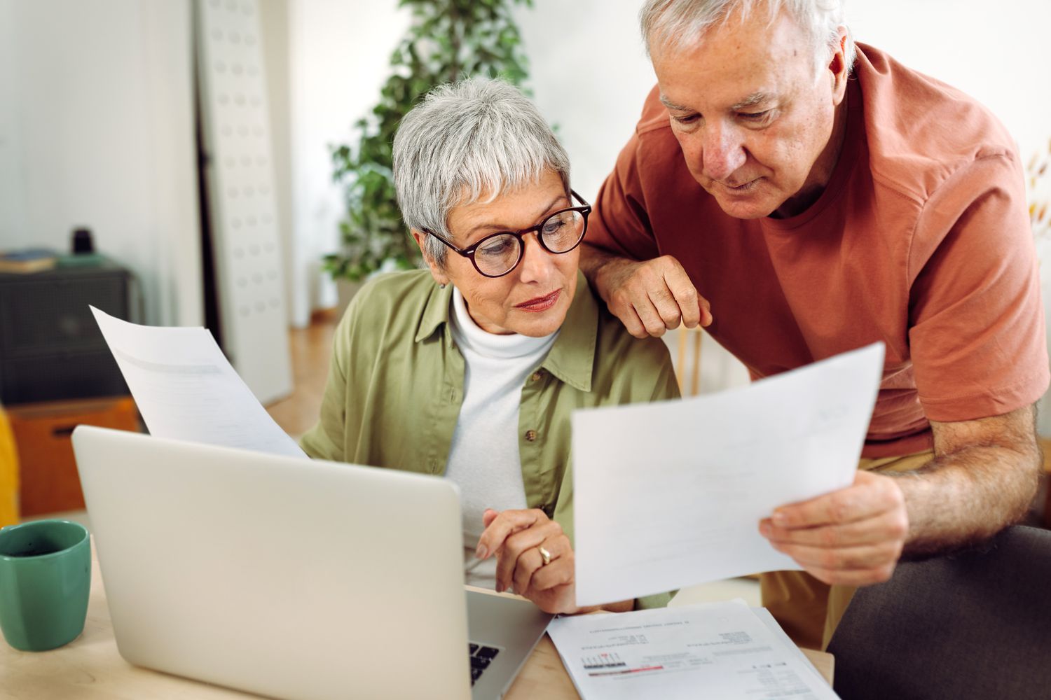 Older couple at their kitchen table, seriously looking at a laptop and documents