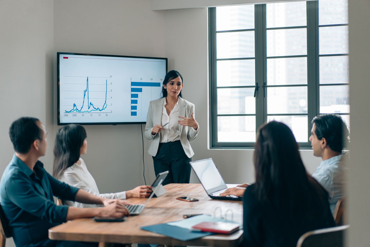 A woman presents charts to a group of four people in an office