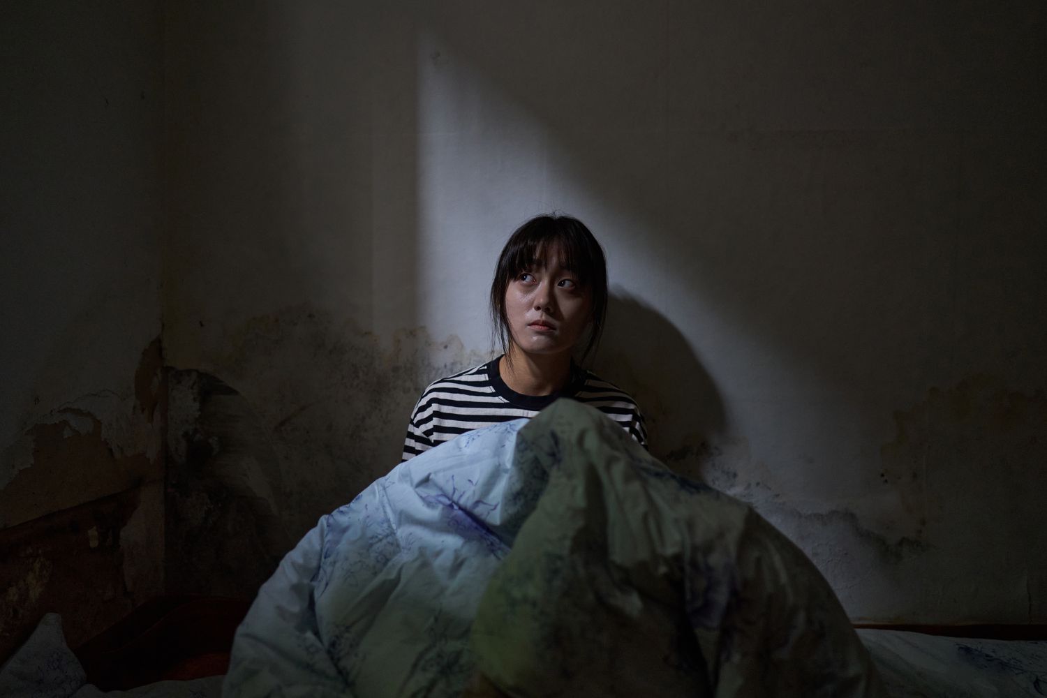 woman sitting on floor against concrete wall with blanket over her body