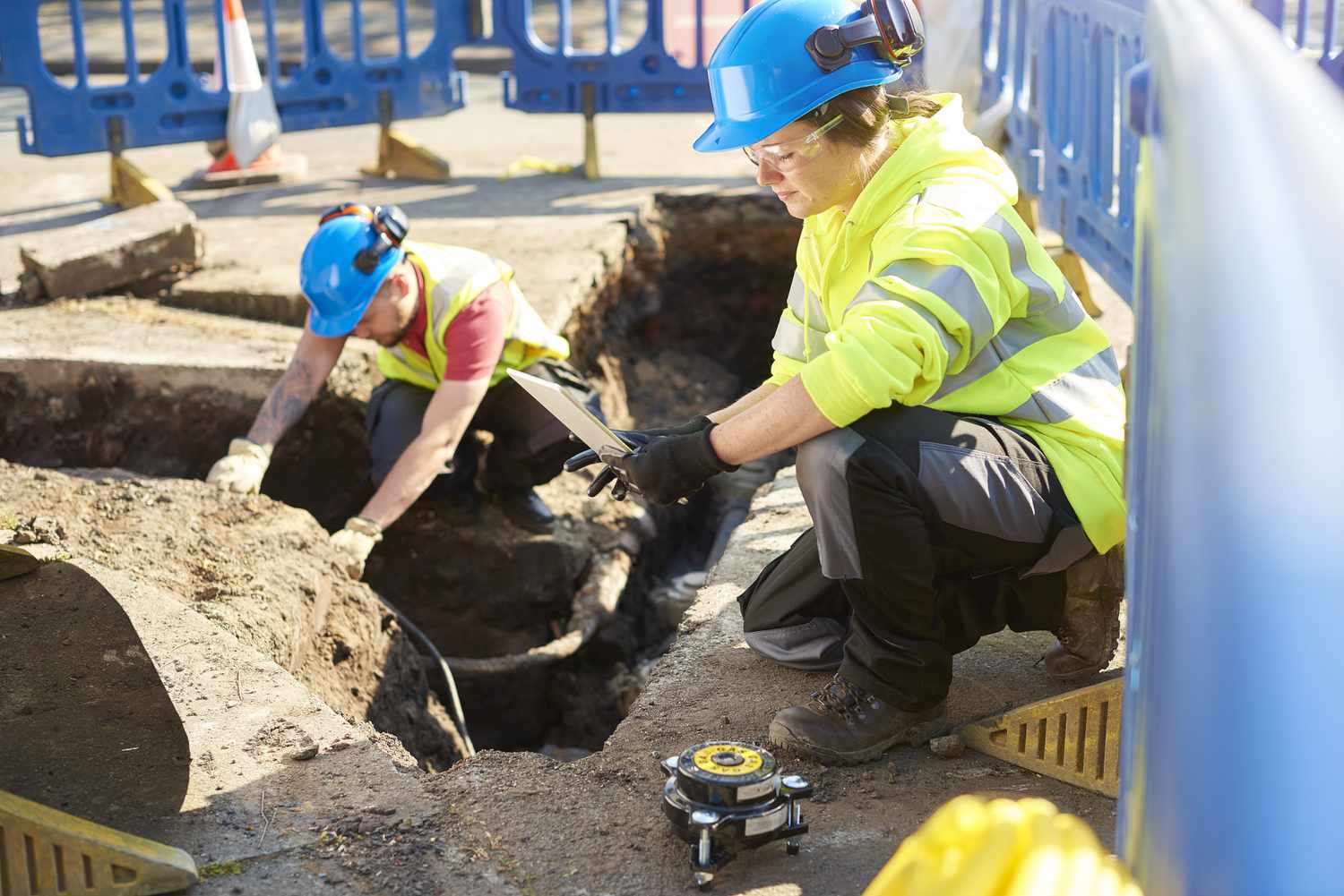Engineers working together to replace an old pipeline in a residential street, one is checking the pipeline's condition and the other noting down details.