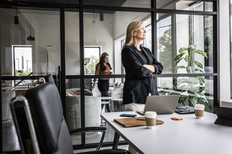 Satisfied looking business woman standing in a conference room and looking out the window.
