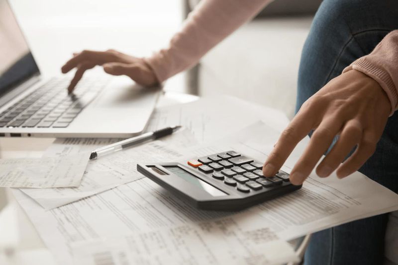 Desktop with documents and woman's hands operating laptop and calculator