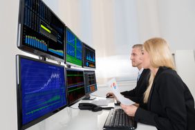 Traders at a desk looking at multiple computer monitors.