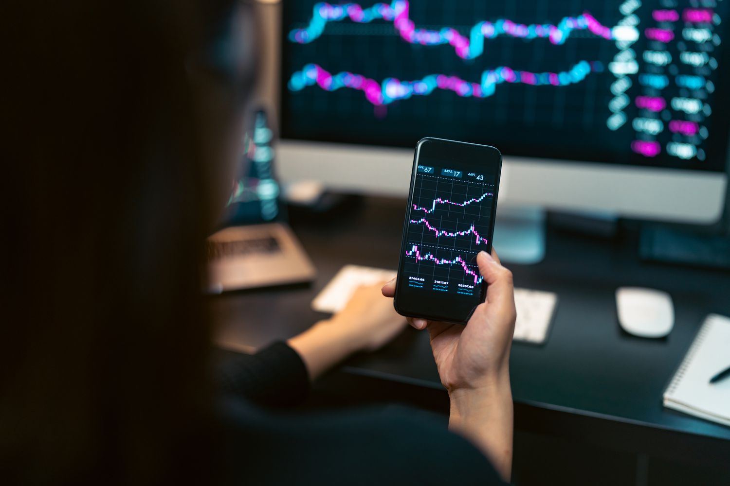 A person looking at a computer and smart phone showing stock data