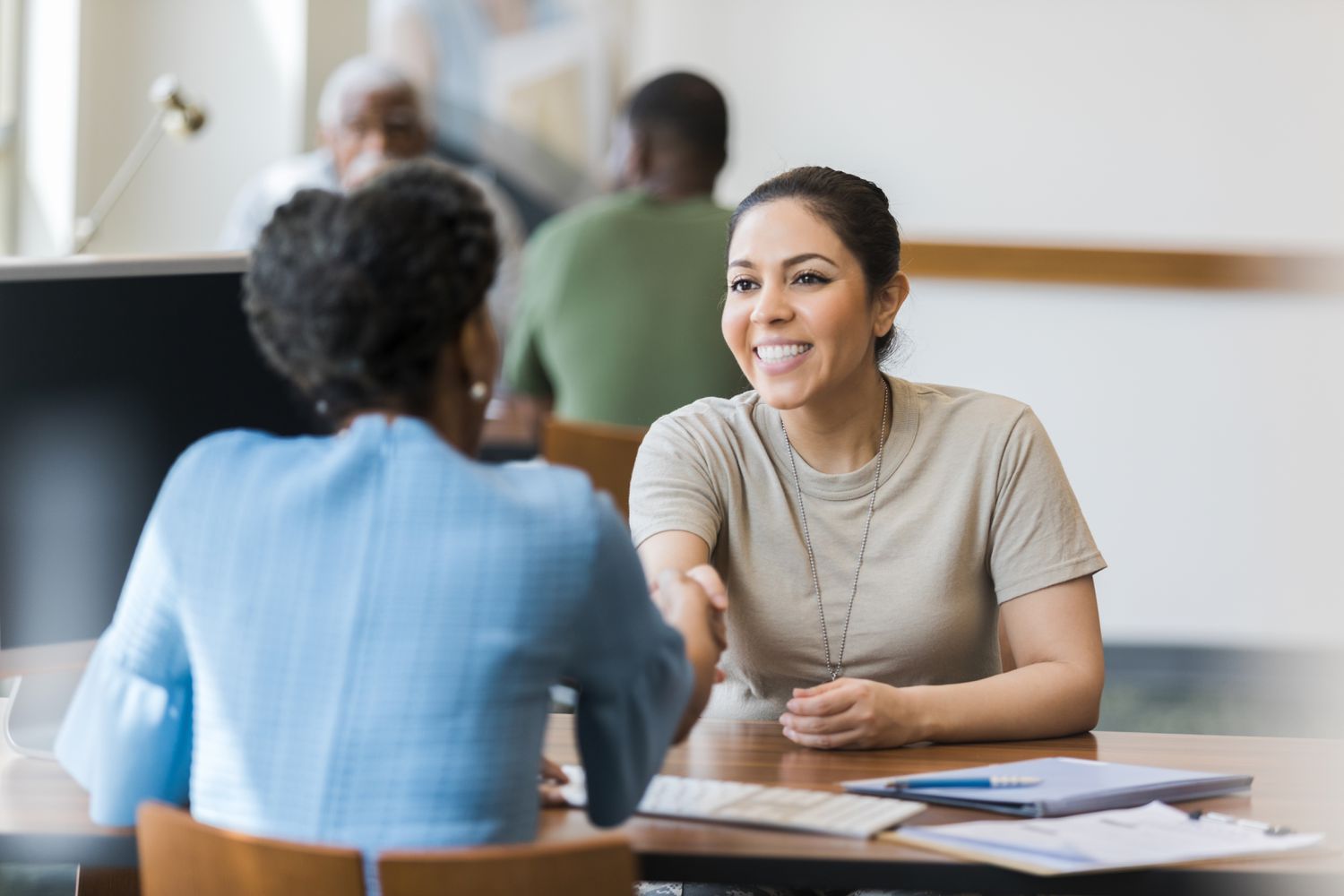 A smiling person opens a CD at a bank, shaking hands with the bank manager.