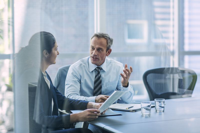 Two business professionals work at a conference table to compile financial information for the company prospectus.