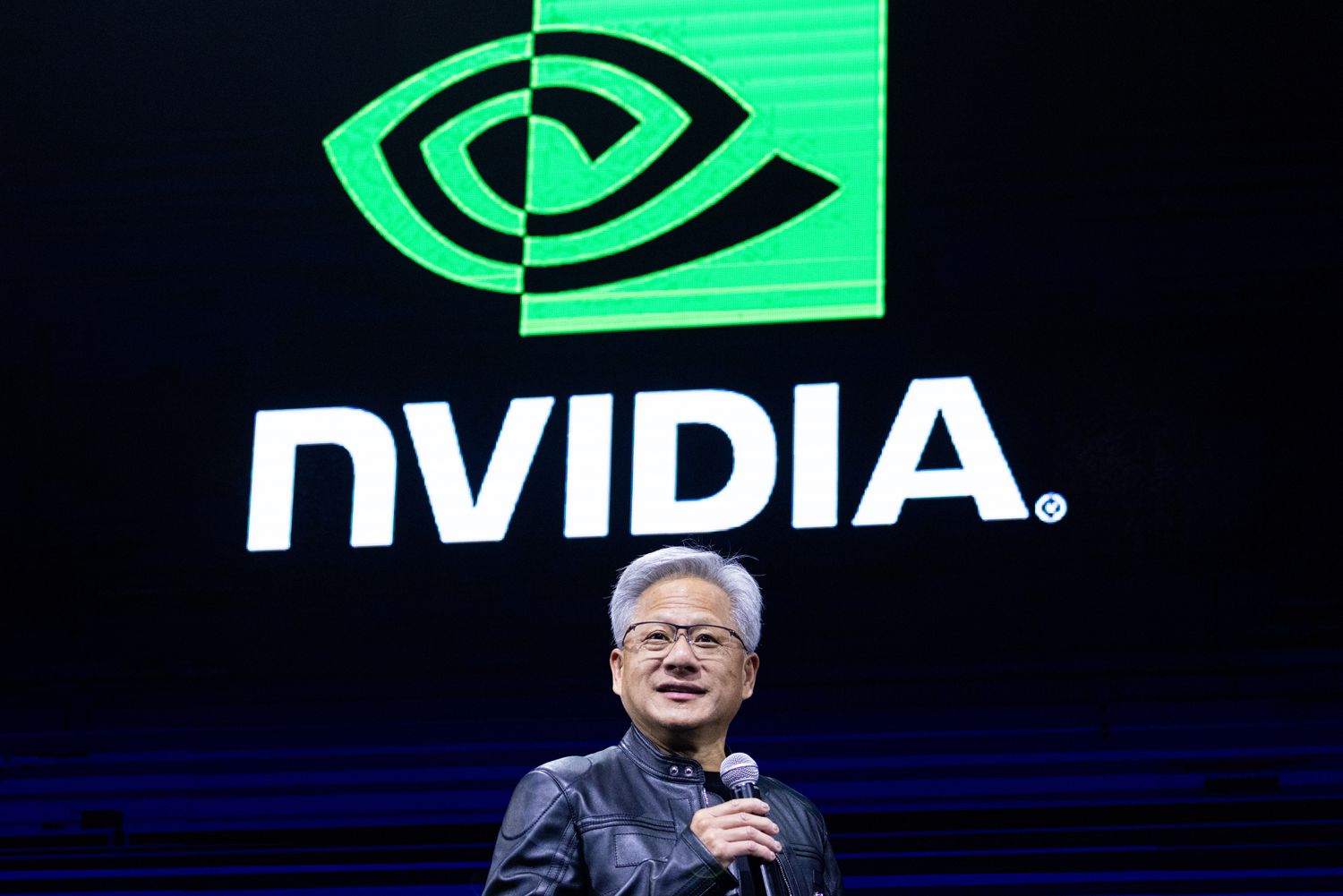 Nvidia CEO Jensen Huang speaks on a stage, with an Nvidia logo on a screen behind him.