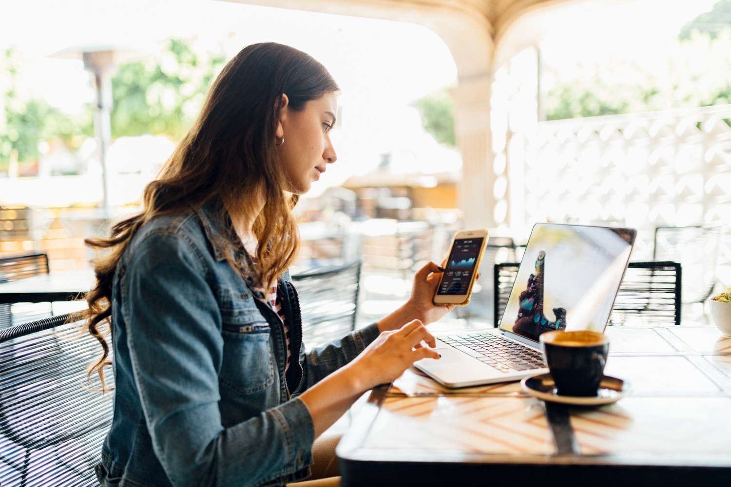 Young woman checking her investments on a smartphone while sitting in a coffee shop.