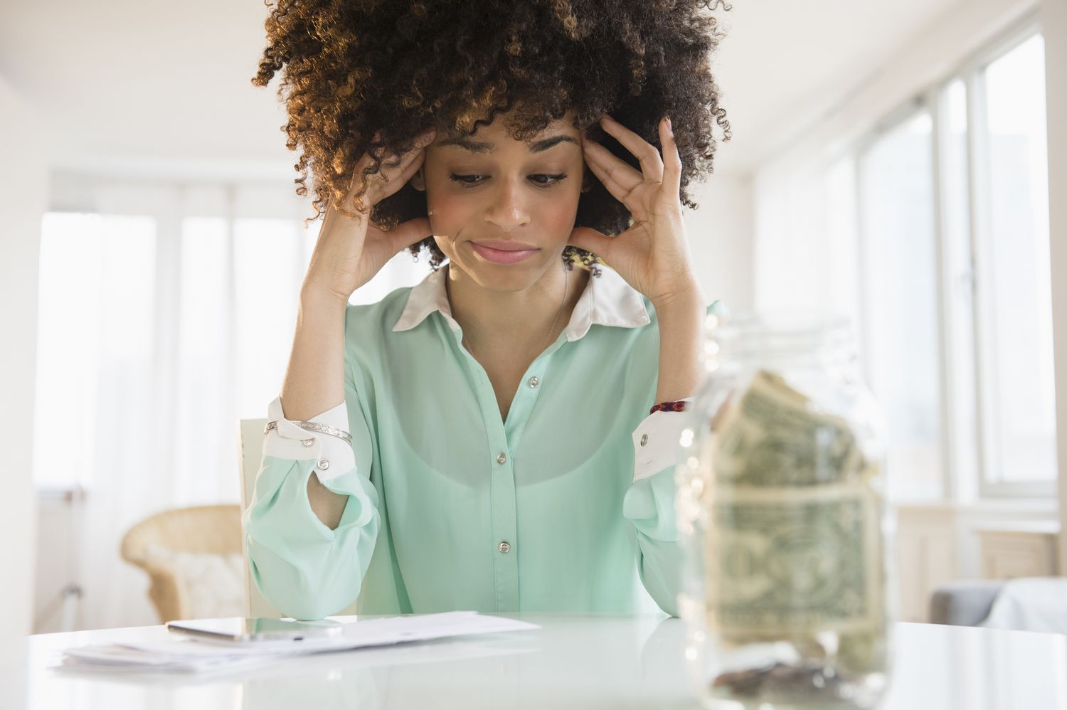 Stressed woman looking at bills and a jar of cash