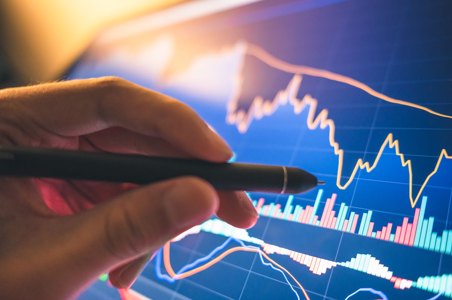 A person's hand holds a pen and points to a screen displaying a chart of the Cboe Nasdaq Volatility Index.