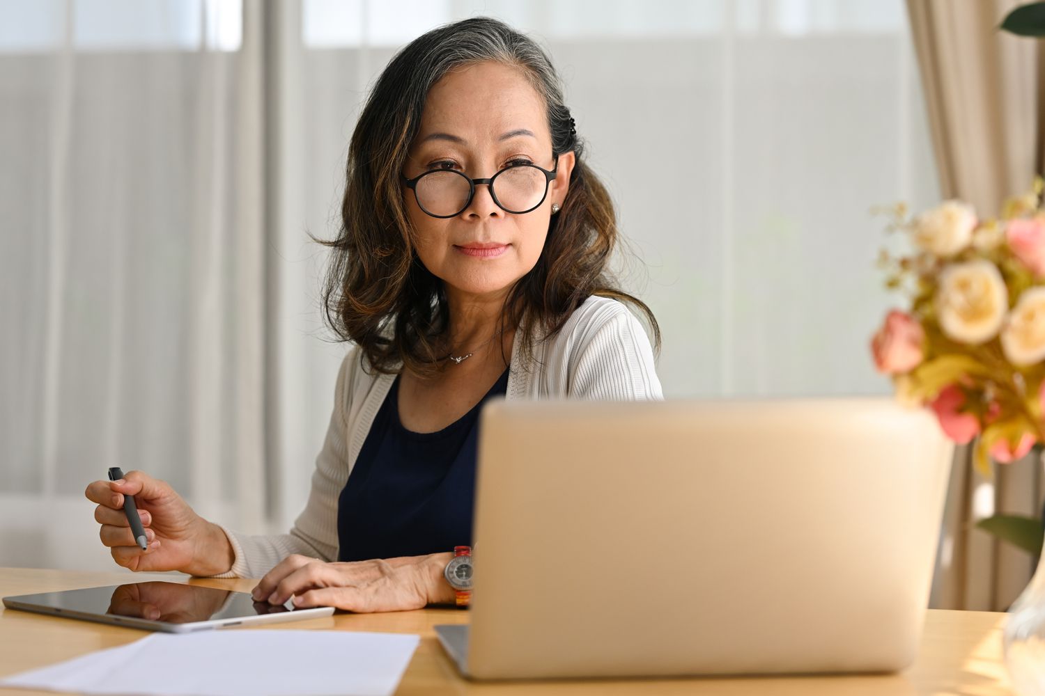 A person sitting at a desk using a tablet and looking at a laptop