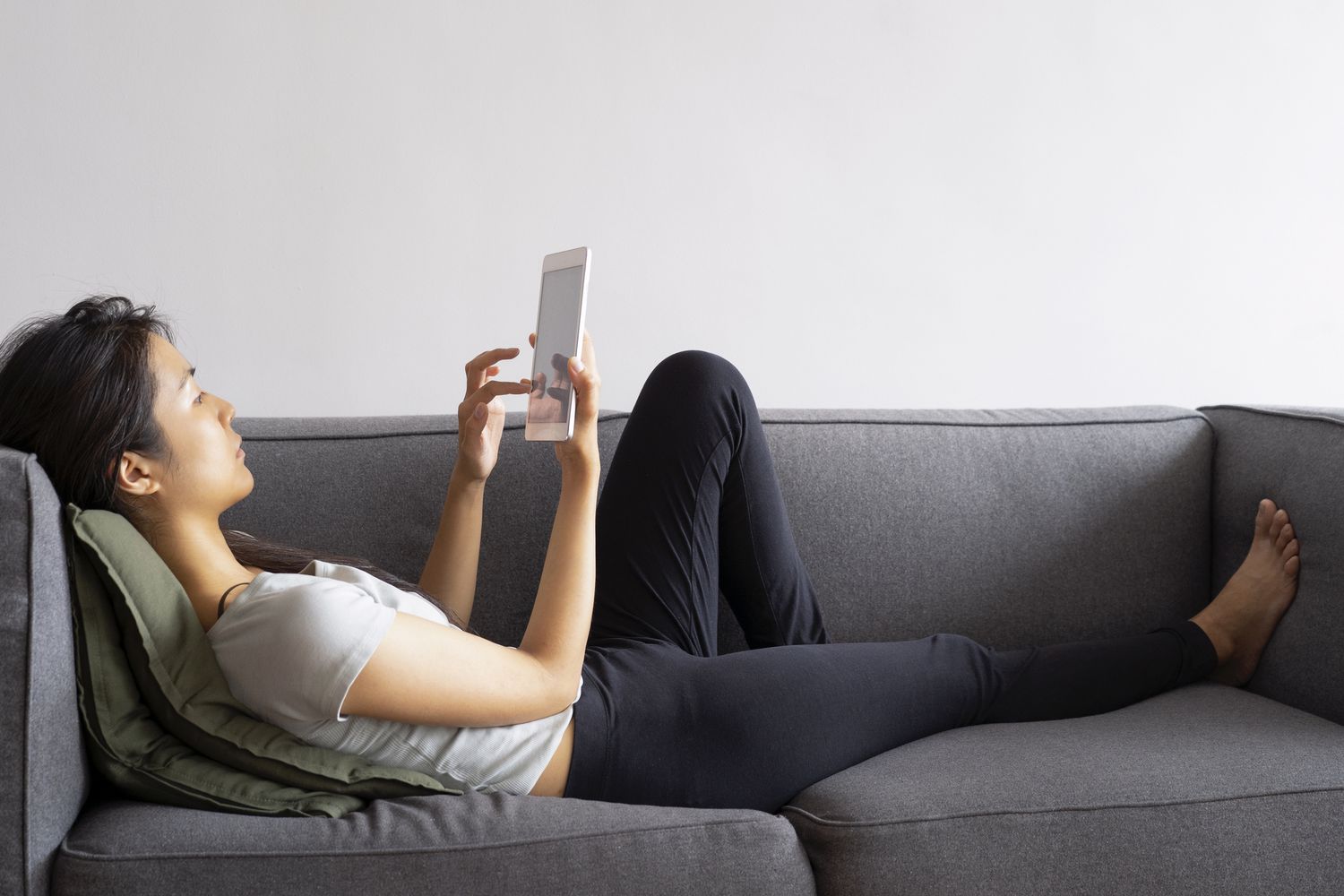 Person laying on a couch while looking at a tablet. 