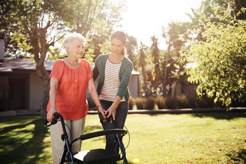 An older woman walks with another woman while using a device to help.