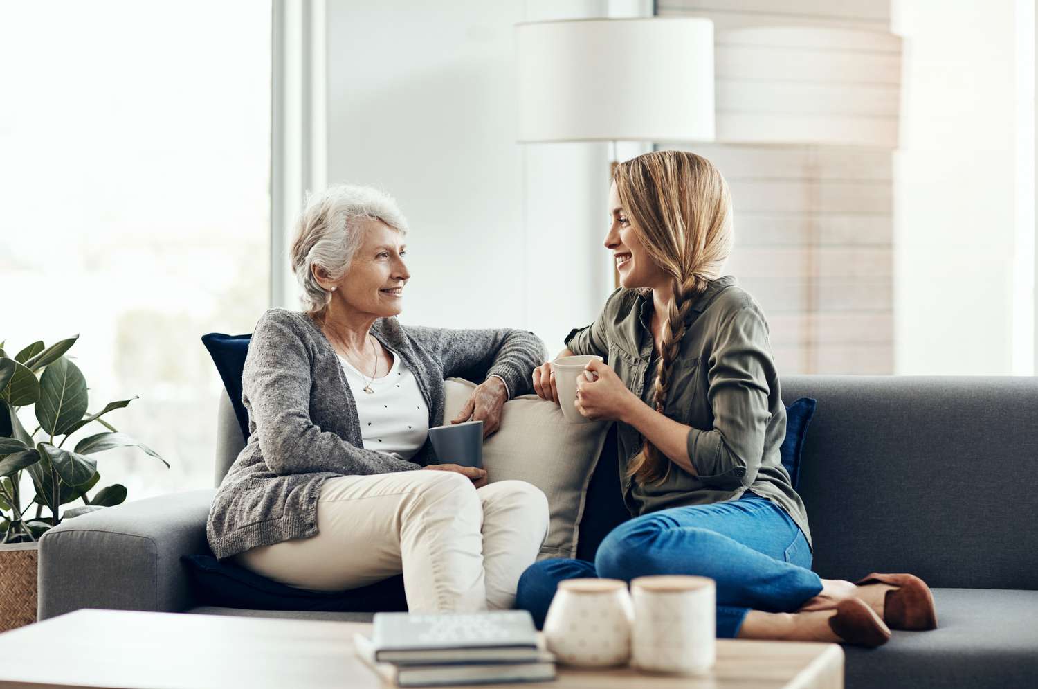 Two women talk on a couch with coffee.