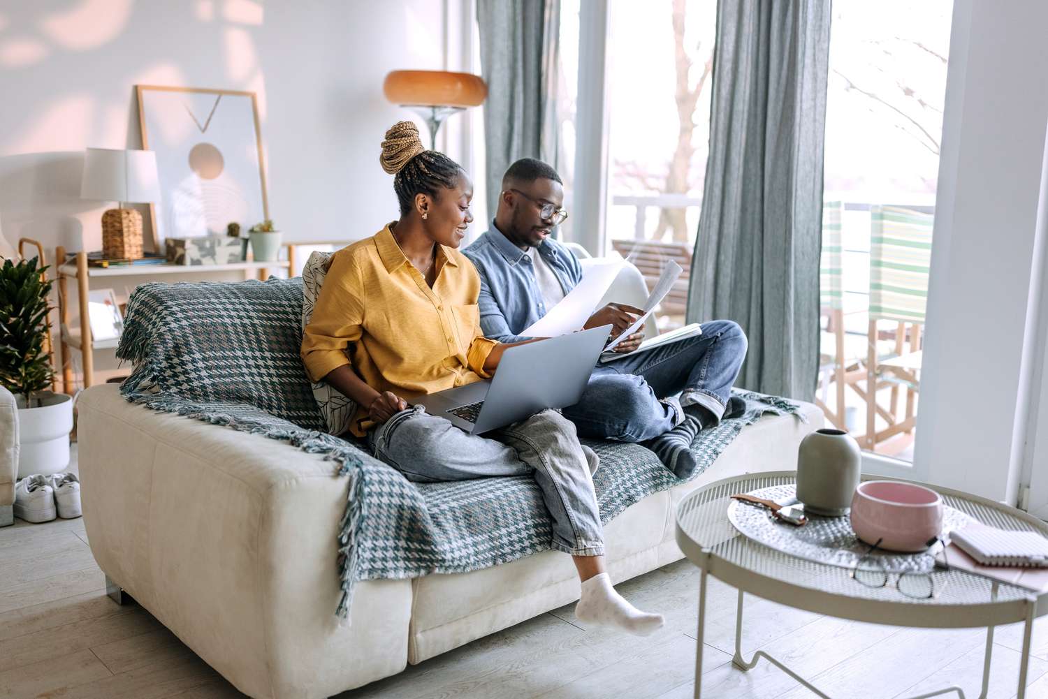 A man and a woman sit on a couch with laptops and paperwork