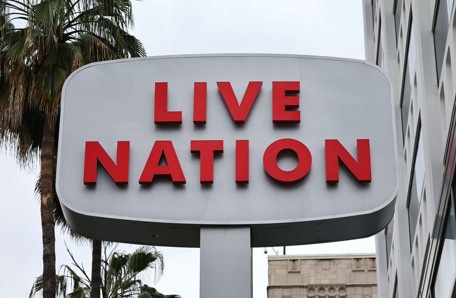 The red Live Nation logo is seen on a white sign in front of a palm tree and cloudy sky.