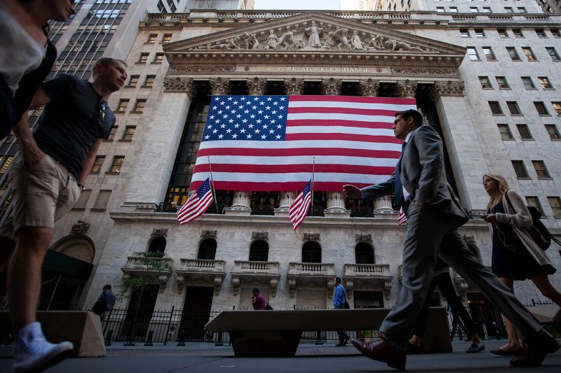 Pedestrians walk past a large American flag hanging outside the New York Stock Exchange building.