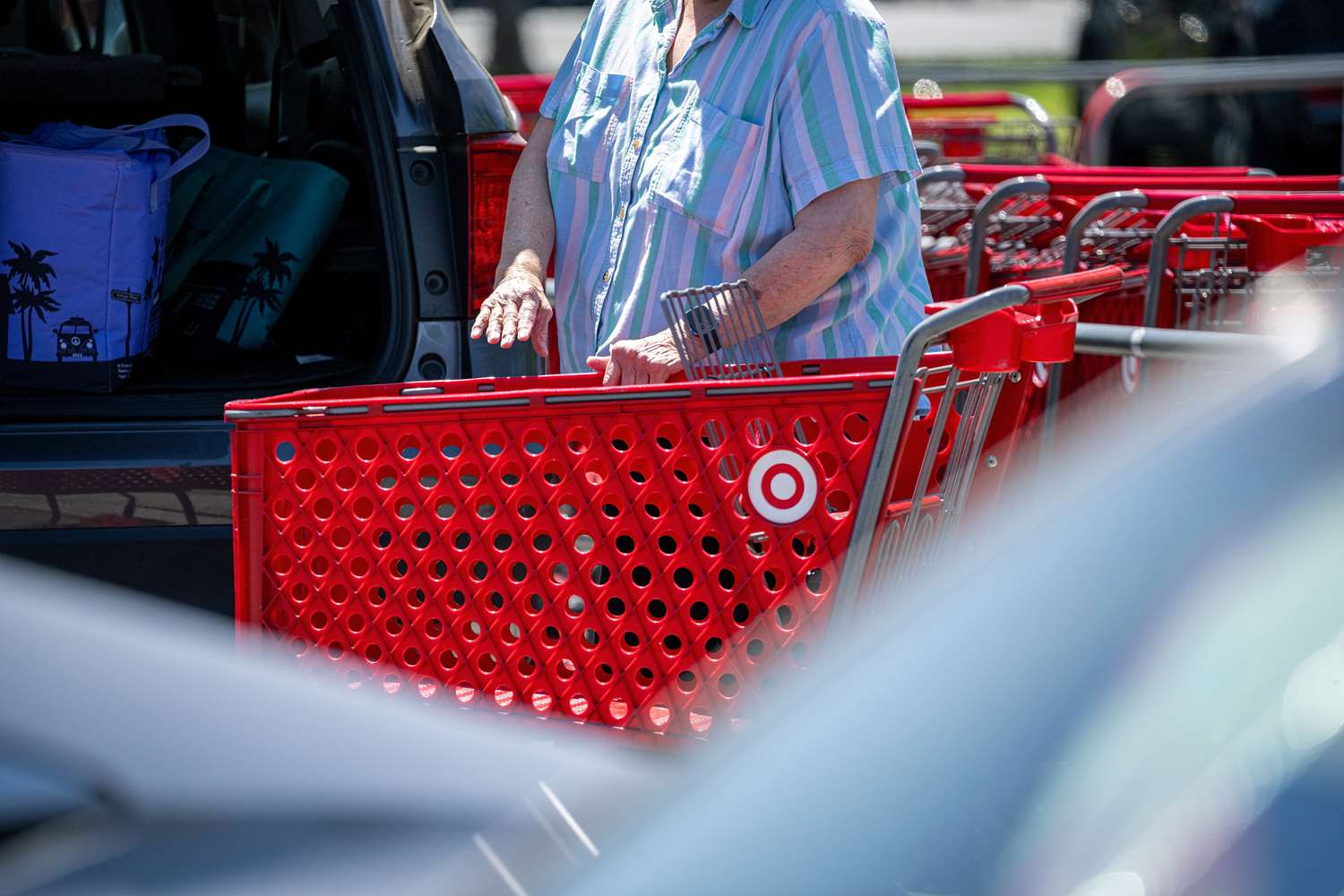A shopper stands near a vehicle with a Target shopping cart.