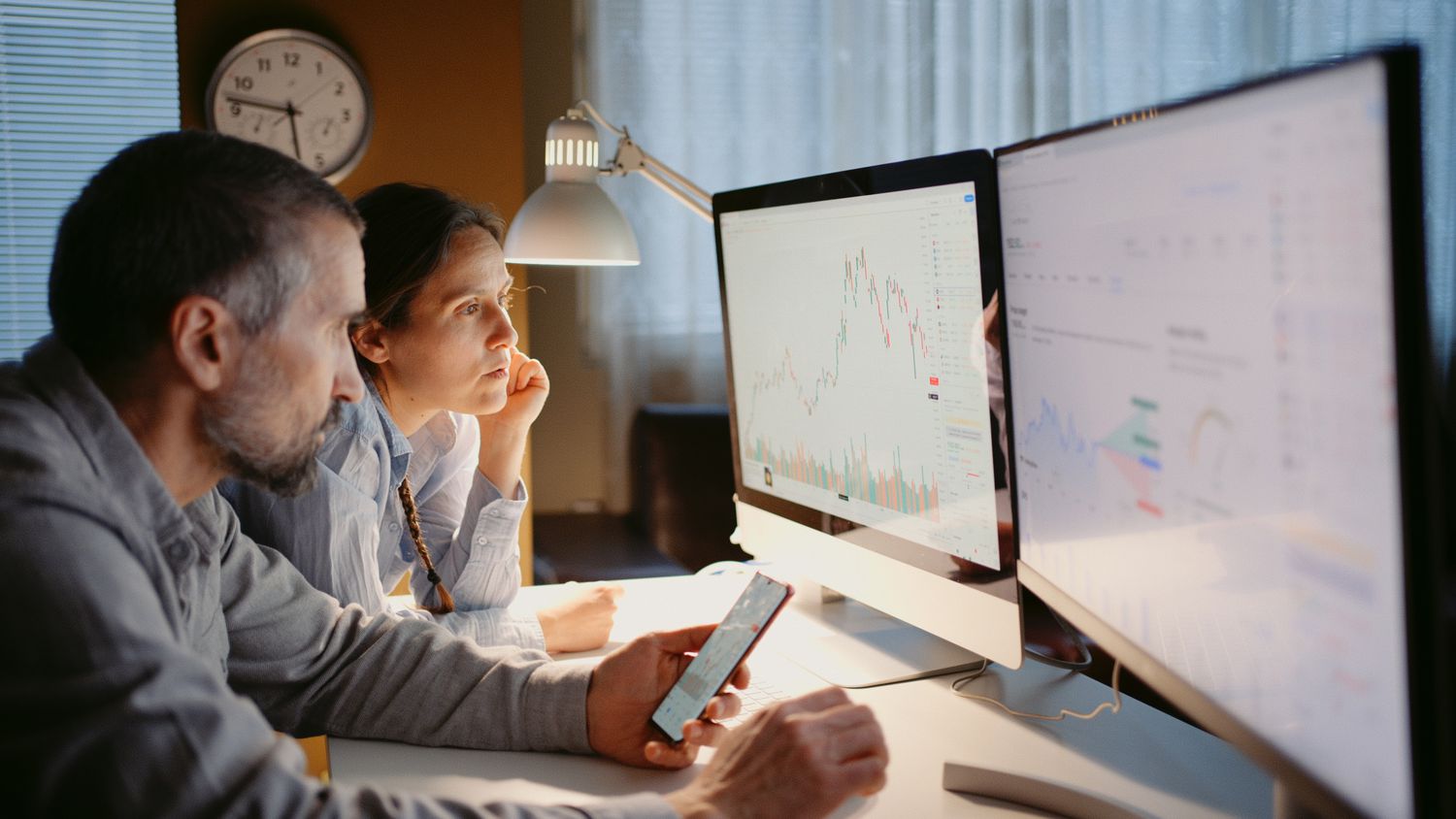 A couple looking charts and other financial data on two computer monitors 