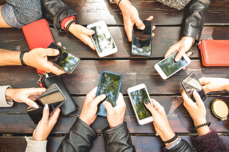 Cropped Hands of Friends Holding Smart Phones on Table