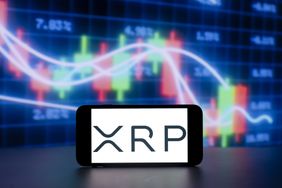 A photo illustration shows the XRP crypto coin logo on a cell phone screen, with stock market charts in the background.