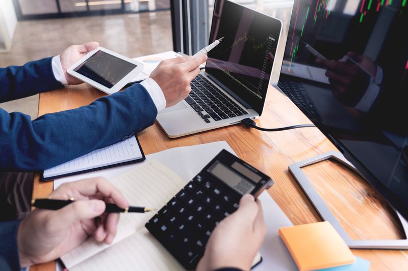 Coworkers discussing over Laptop In Office using a calculator.