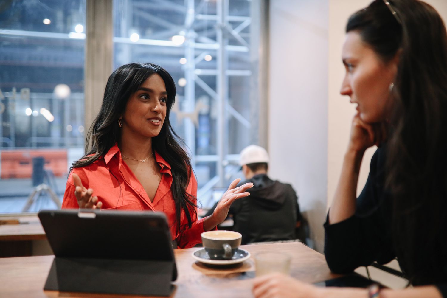 Two women sit at a coffee shop table with a tablet