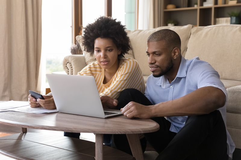 Young Black couple analyzing their household budget on a laptop in their living room.