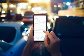 Human hands checking financial trading data on mobile phone while walking to car in parking lot