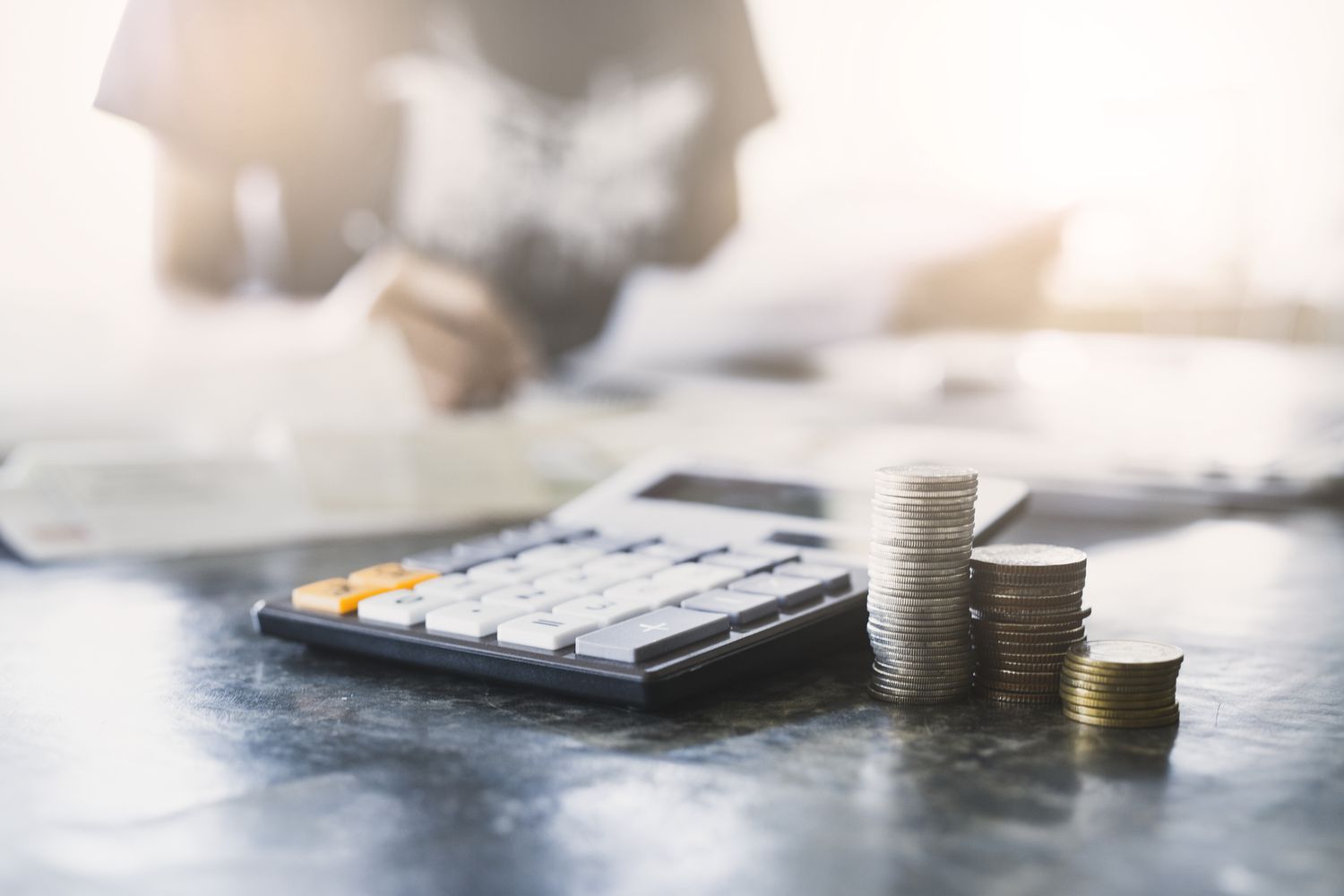A close-up of calculator and coins with a young woman analyzing financial data.