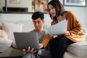 Young couple discussing savings accounts while using laptop
