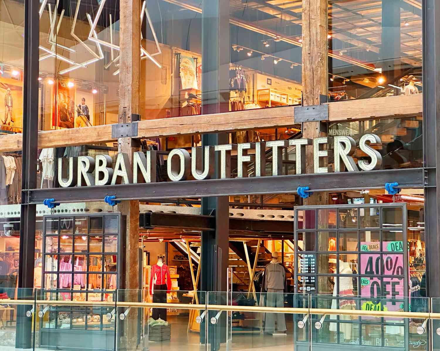 An Urban Outfitters sign is seen above the entrance to a brightly lit store with clothes inside.