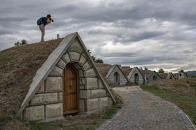 Person photographing small, triangular-roofed buildings extending along a cobblestone pathway