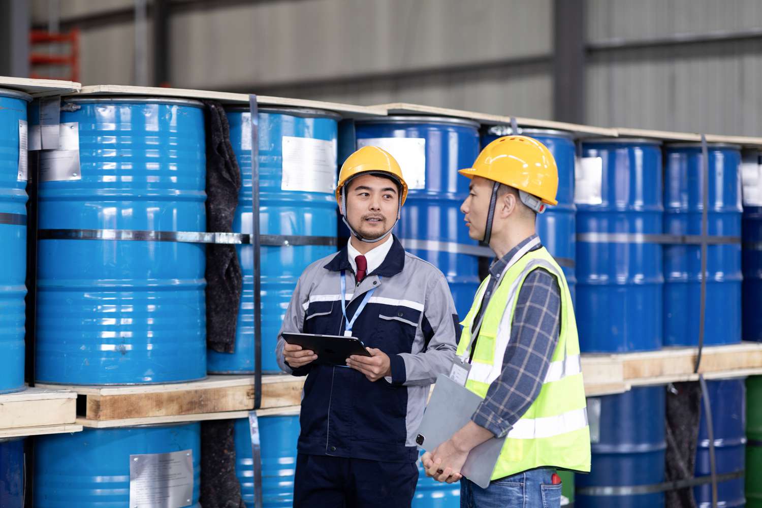 Two engineers walking together with oil barrels in the background at an oil blending factory.