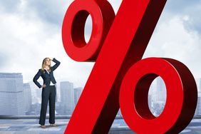 Businesswoman with hand on top of head is looking up at red percentage sign.