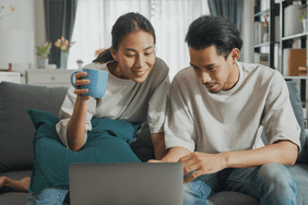 Young couple sitting on their sofa and looking together at mortgage rates on a laptop