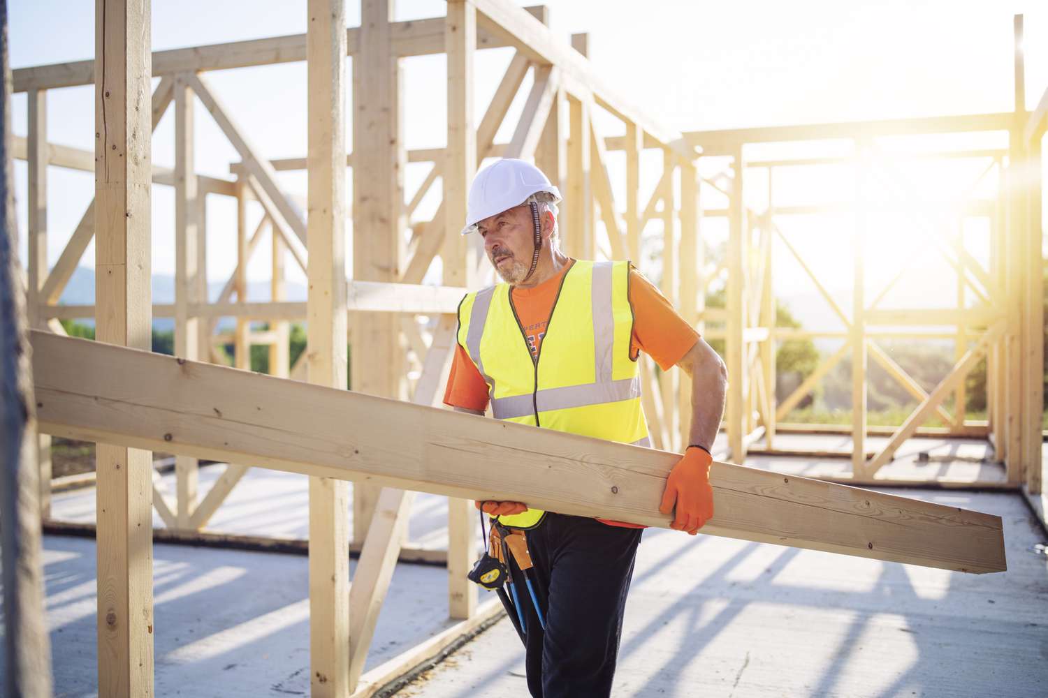 Construction worker carries a beam while working on an unfinished wooden structure