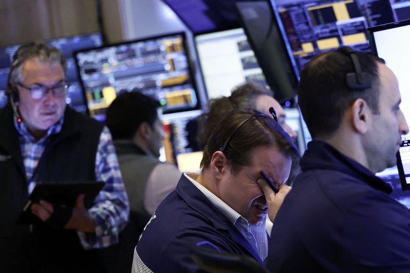 Traders work in front of computers on the floor of the New York Stock Exchange, one with his head in his hands.