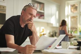 A middle-aged man sorts bills in his kitchen. 