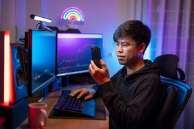 Young asian male trading and currency trading app on his smartphone 
