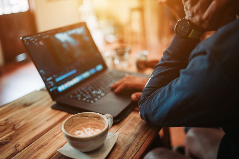 Person sitting at a table working on a laptop with a cup of coffee beside them.