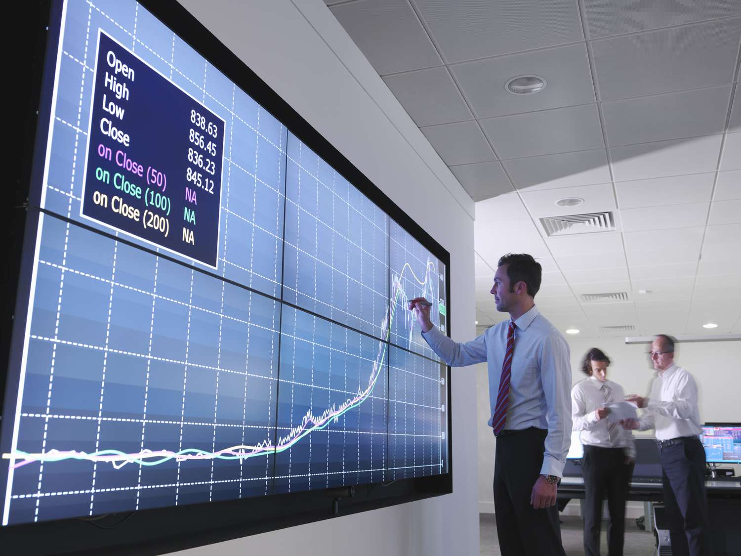 Man in trading room evaluating trends of an asset on a big screen