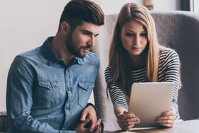 Young couple sitting at home together and looking seriously at a tablet