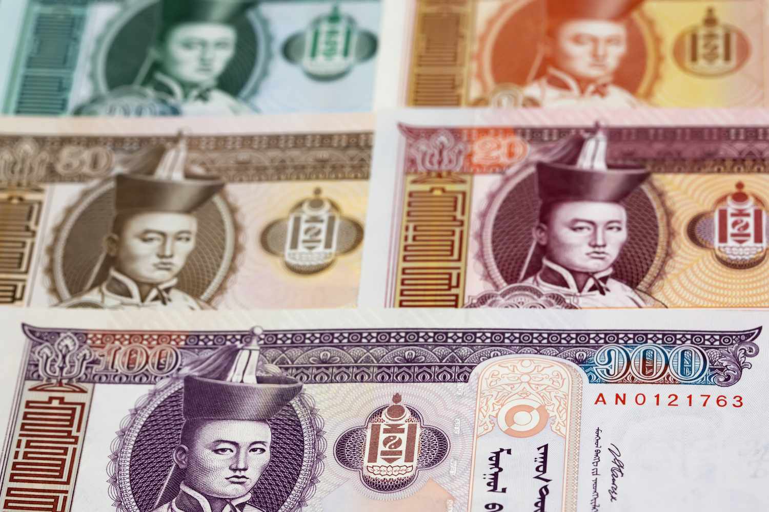 A close up of a collection of Mongolian Tugrik banknotes featuring a past ruler spead on a surface.