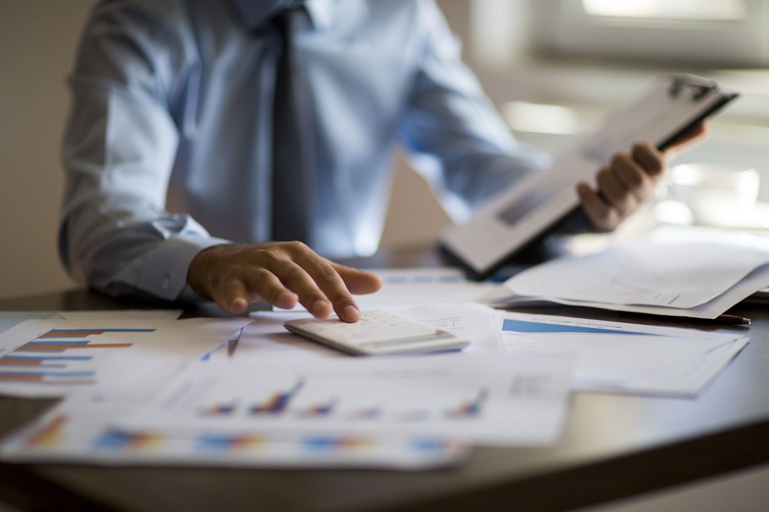 Cropped body photo of businessman using calculator with papers of financial graphs on his table