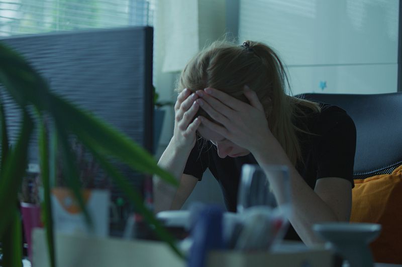 A stock image of a woman holding her head in her hands while at work. 