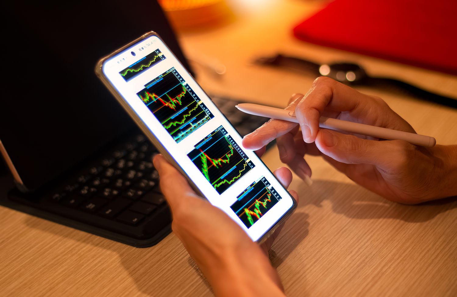 Hands of a person holding a mobile phone with charts displaying on the screen