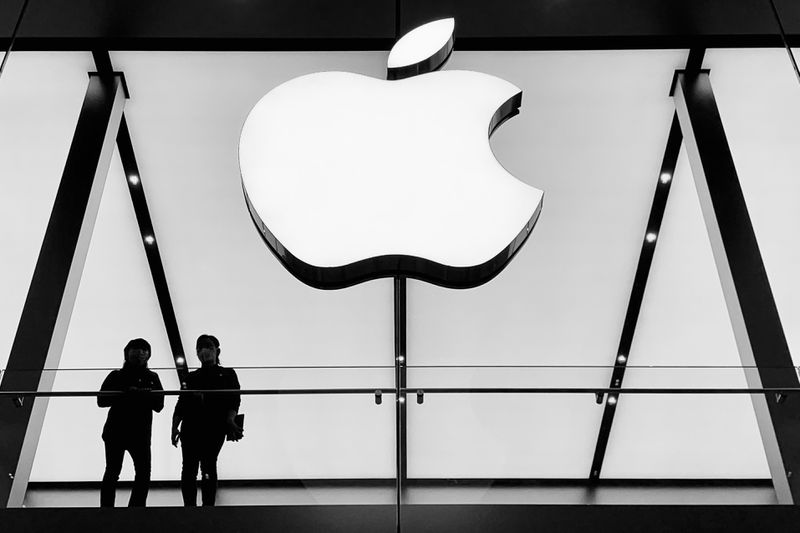 Two people looking through a window with the Apple logo above them.