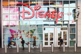 People walk in front of the Disney store in Times Square, with a red Disney logo above the door.