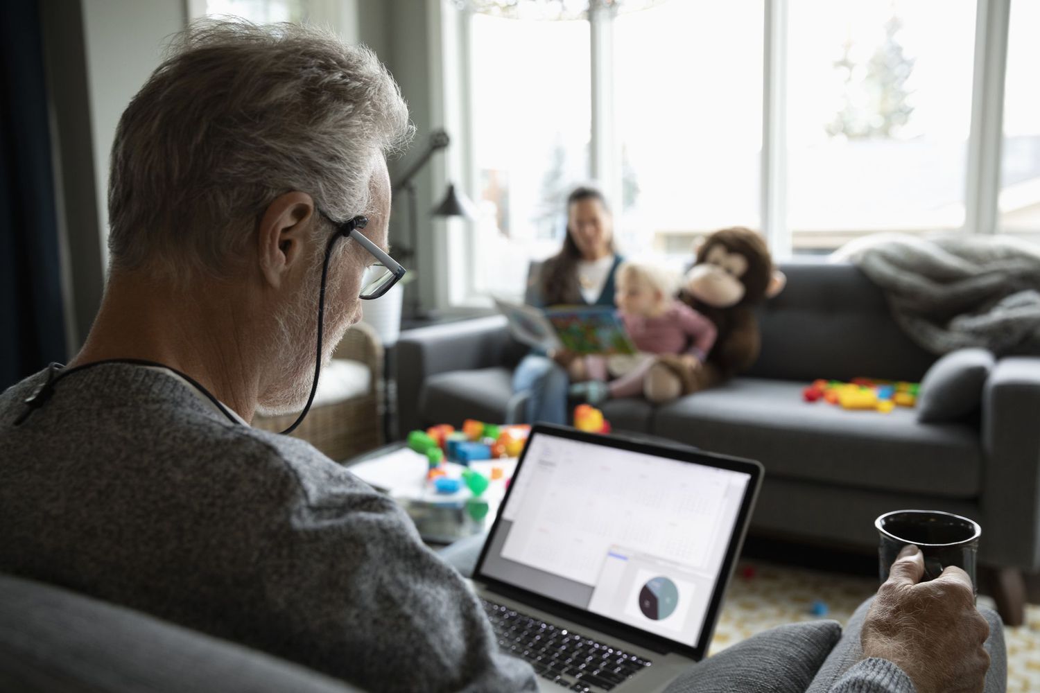 Worker on laptop with mug with family in background